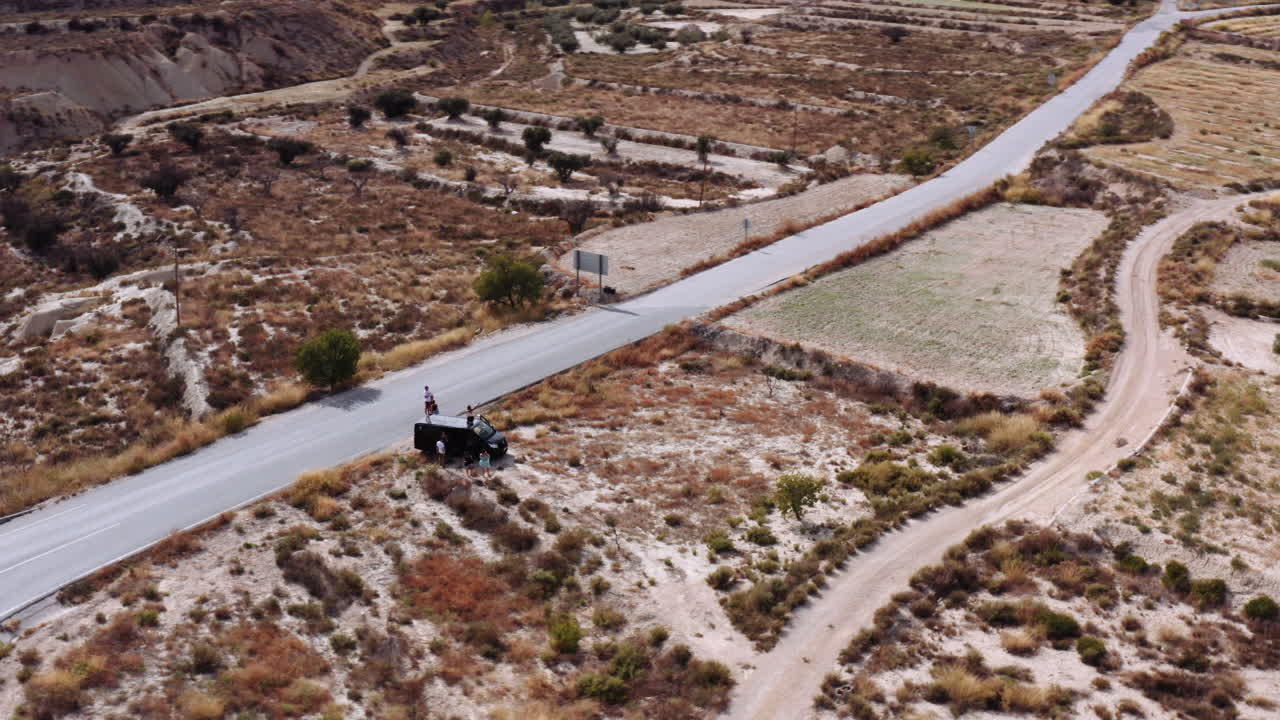 un dron dando vueltas alrededor de un grupo de amigos en un viaje por carretera, descansando al lado de la carretera junto a su coche negro en un hermoso paisaje de pastizales en las afueras de murica, españa