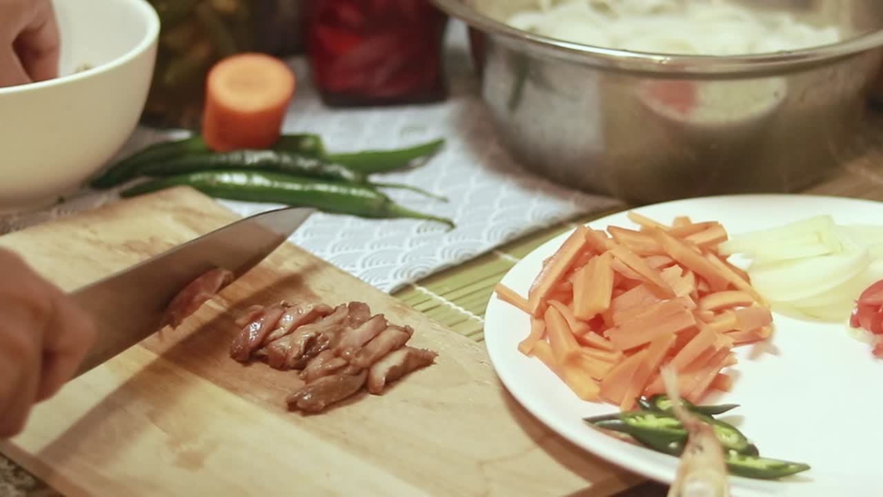 Hand slicing marinated pork meat into strips and setting it aside, candid kitchen scene of preparing ingredient for cooking