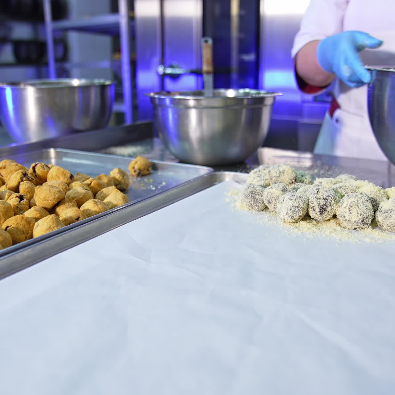 Confectionery worker covers the biscuits with sprinkling. Female hands take the sweets, puts them into a metal bowl, mixes and puts them on a tray