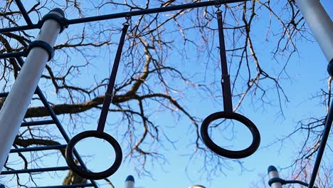 gymnastic rings move in the wind with trees and blue sky on the background, steady close up shot