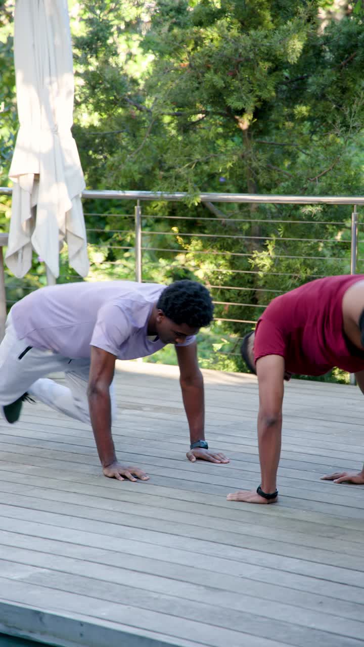 Video vertikal: Teman-teman pria yang beragam memulai latihan dengan melakukan push-up, squat, tos di atas dek