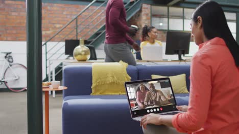 mujer biracial usando una computadora portátil para una llamada de video, con diversos colegas de negocios en la pantalla