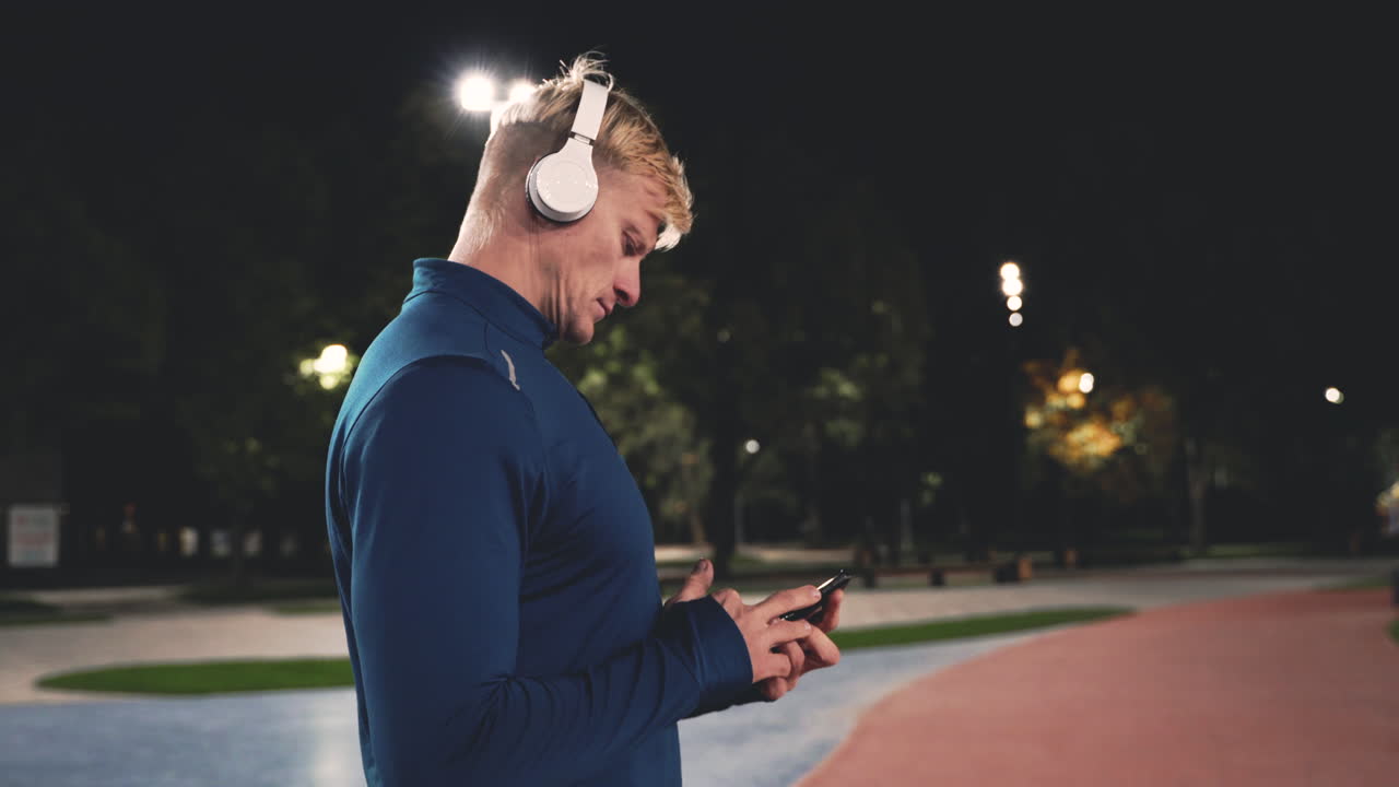 deportista concentrado usando teléfono móvil para activar los auriculares bluetooth y luego comenzar a correr en el parque por la noche