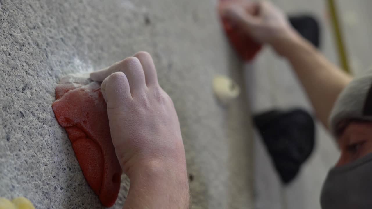 Rock climber climbing an indoor rock wall using athletic chalk for grip.