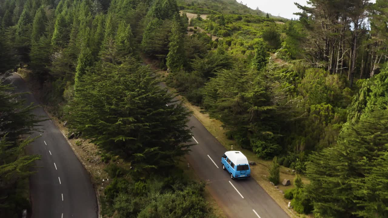 Aerial follows a VW-Camper van that drives on a empty road on Madeira, Portugal