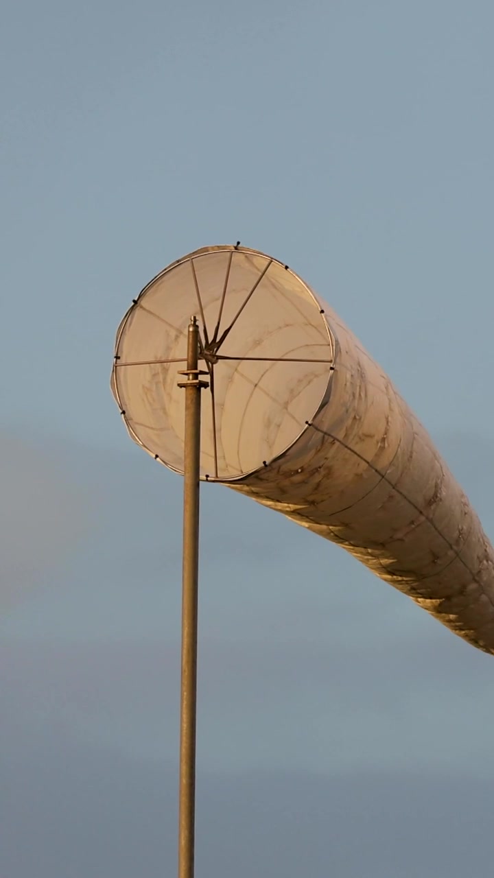 Una manica a vento di tessuto bianco ondeggia su un palo su uno sfondo di cielo azzurro limpido
