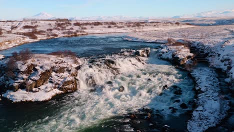 Establishing-drone-shot-of-beautiful-waterfall-and-river-in-Iceland-during-winter-snow