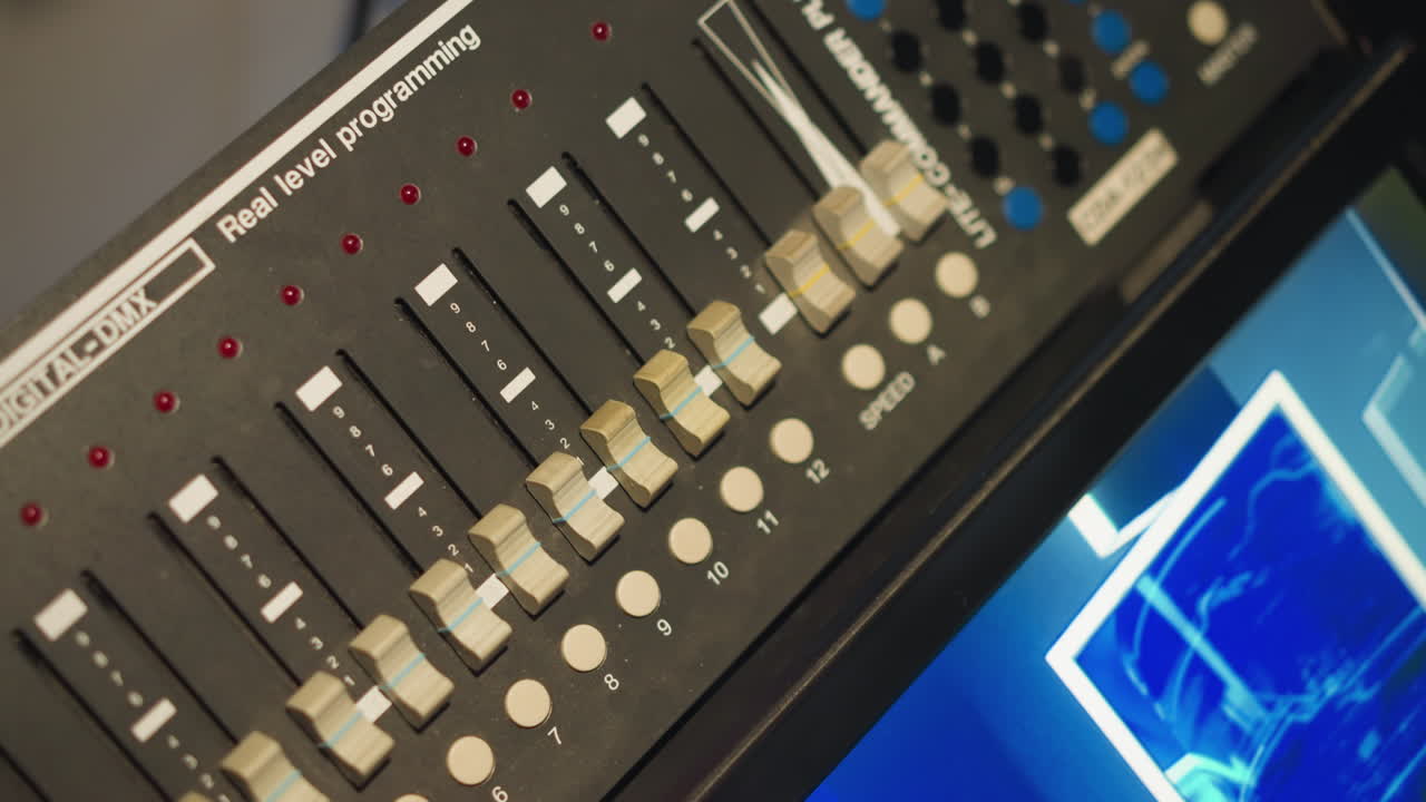 Person adjusting sliders on lighting control panel, programming real-time lighting levels. Close-up shot of hand manipulating faders on control board with digital display