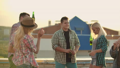 fife young american people move in a dance on the party on the roof. they have fun smile and drink beer.