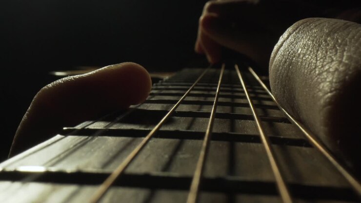 Karanlık stüdyoda müzisyenin parmak tekniğiyle gitar telleri çaldığı makro yakın çekim.