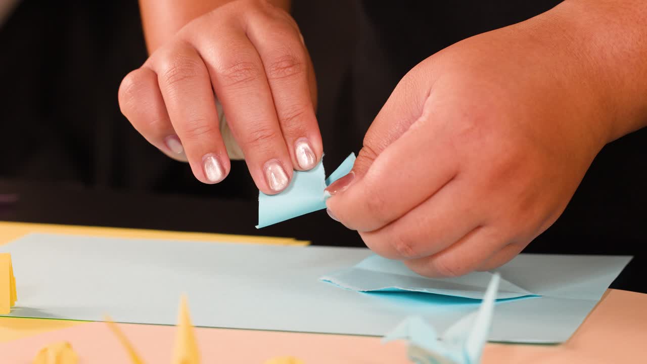 Close-up shot of hands folding blue paper into origami shapes on a studio table
