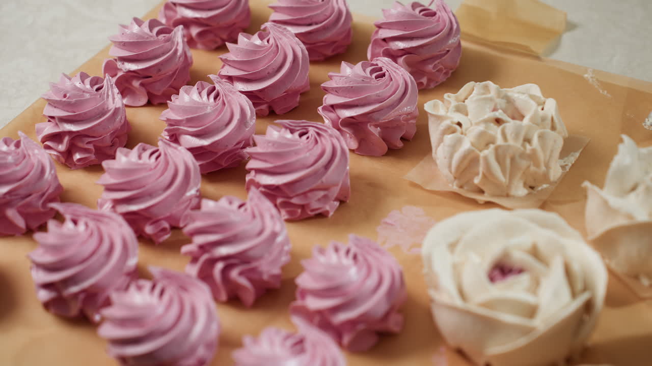 Close up of beautifully arranged pink swirl cupcakes and flower-shaped white frosting cakes resting on parchment paper, showcasing elegant icing textures and handcrafted dessert artistry