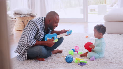 young black father palying ukulele with son in sitting room