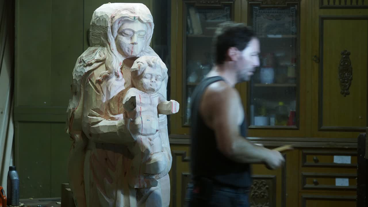 Artisan carefully carves the wooden Madonna and Child statue inside a workshop, shaping sacred details with precision and devotion in traditional craftsmanship