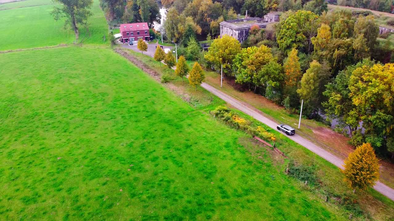 Aerial view above the belgian countryside with a car driving up a dirtroad towards a hidden historical fortress. (Fort of Haasdonk)