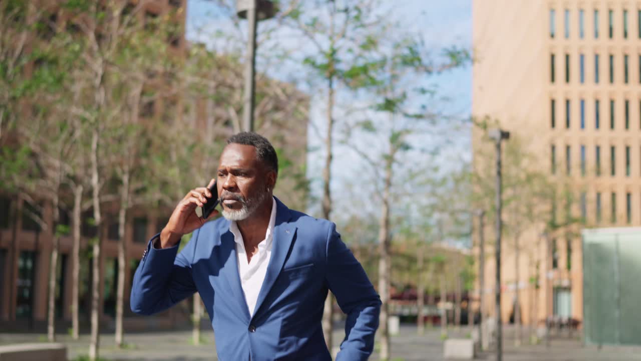 Un uomo d'affari afroamericano che cammina e parla al telefono in città