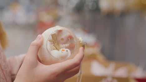 the buyer holds a toy snowman in his hands - chooses decorations for the christmas tree