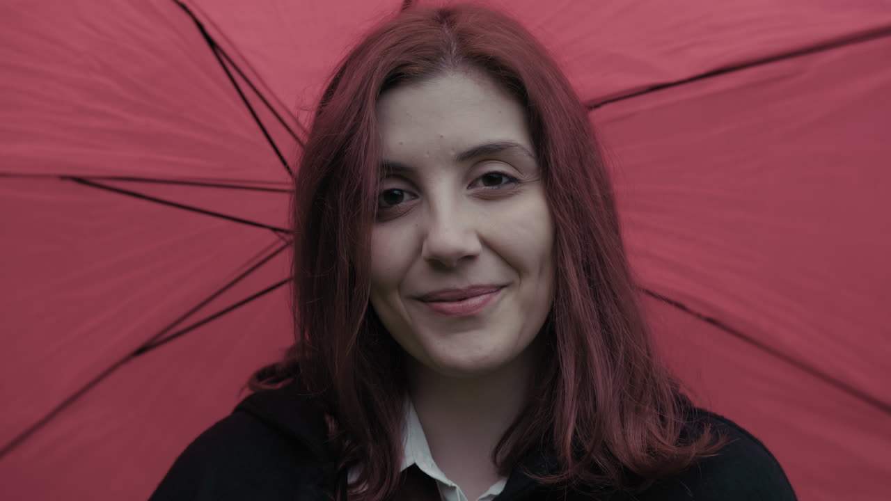 una mujer italiana feliz sonríe de cerca con un paraguas rojo giratorio durante la lluvia