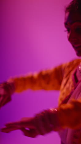 vertical video close up on hands of female kathak dancer performing dance wearing traditional indian dress against purple background