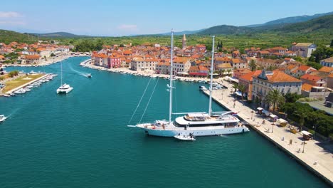 panorama of a coastal town with many houses with red roofs, surrounded by the sea and mountains with yachts in marina bay and bell tower and walking peoples