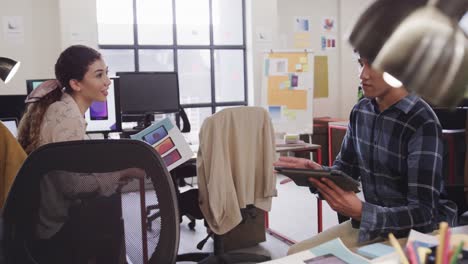 Two-happy-diverse-creative-designers-in-discussion-at-tablet-in-casual-office,-slow-motion