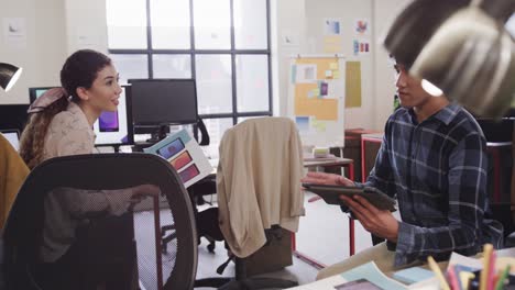 dos diseñadores creativos felices y diversos en discusión en una tableta en una oficina casual, cámara lenta