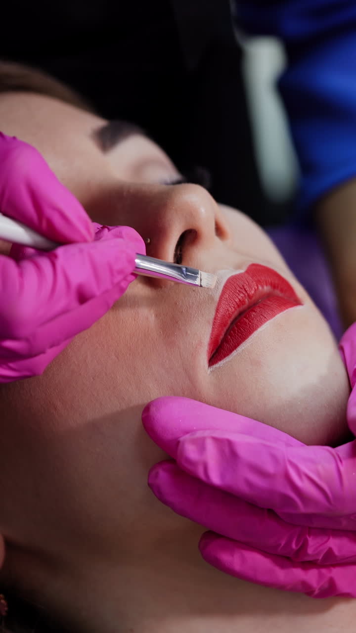 Beautician paints contour on woman's lips. Preparation before the permanent makeup on lips. Plastic medicine and cosmetology. Vertical video
