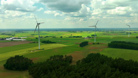 Luftaufnahmen-Zeigen-Drei-Windturbinen,-Die-Hoch-über-Einer-Weiten-Ländlichen-Landschaft-Mit-Feldern-Und-Bäumen-Stehen