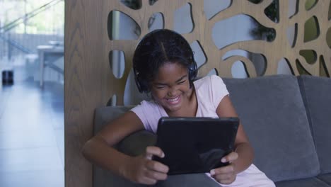 African-american-girl-smiling-while-using-digital-tablet-sitting-on-the-couch-at-hospital