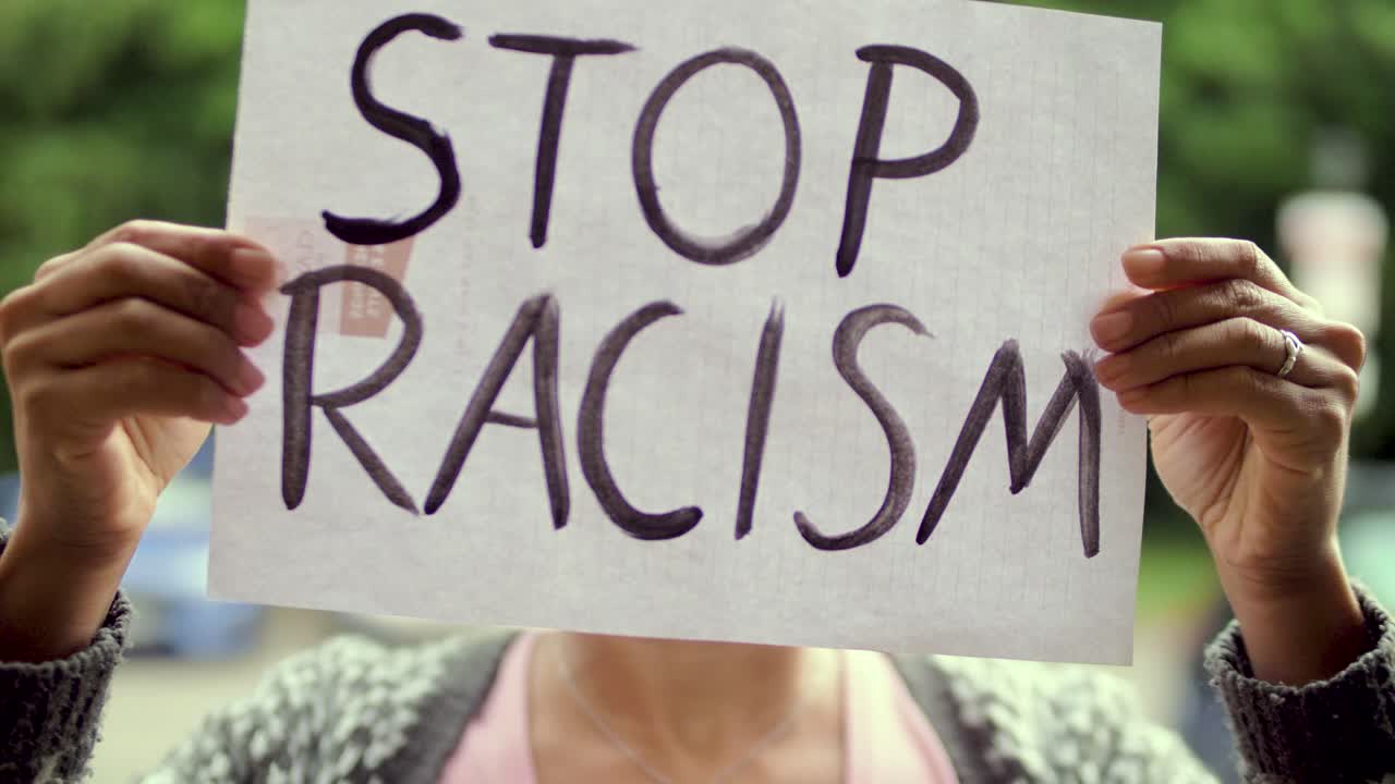 Young black Woman holds &amp;quot;Stop Racism&amp;quot; Poster in front of her Face