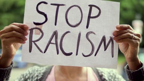 young black woman holds "stop racism" poster in front of her face