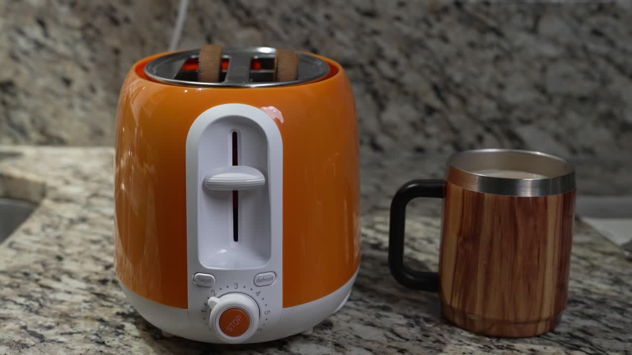 Hand presses the button for an orange toaster on a marble counter