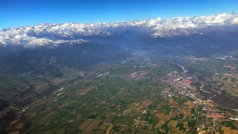 Aerial-footage-of-a-green-valley-under-the-alps-covered-in-snow