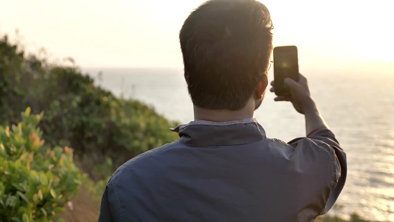 A young male or tourist taking a picture of a sunset.