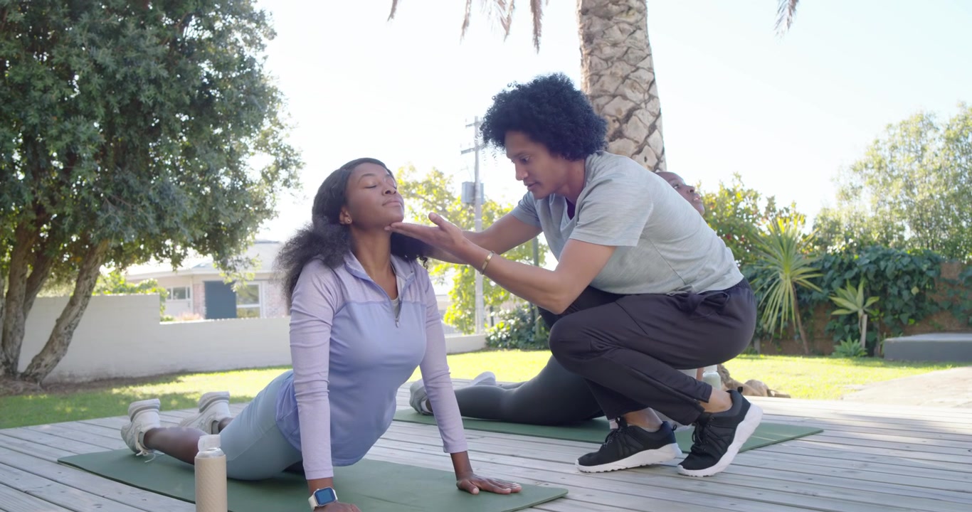 Istruttrice afroamericana che guida le donne dalla posizione del bambino a quella del cobra su tappetini, allineando il collo.