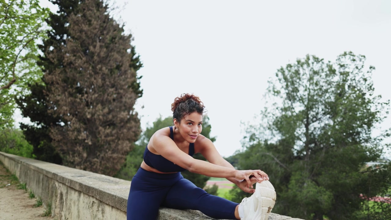 Athletic Woman Stretching Her Leg on a Wall in a Park
