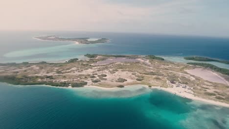 vista aérea isla tropical rodeada de sombras de agua de mar azul y arrecife de coral, los roques