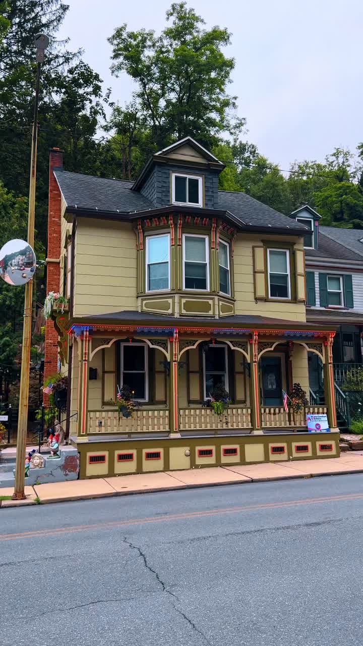Jim Thorpe, AS, 2 Juli 2025: Bangunan arsitektur Victoria bersejarah dengan lis teras berornamen. Sebuah rumah Victoria hijau zaitun berlantai dua yang menampilkan detail ukiran kayu rumit, atap pelana, dan teras depan yang dihias.