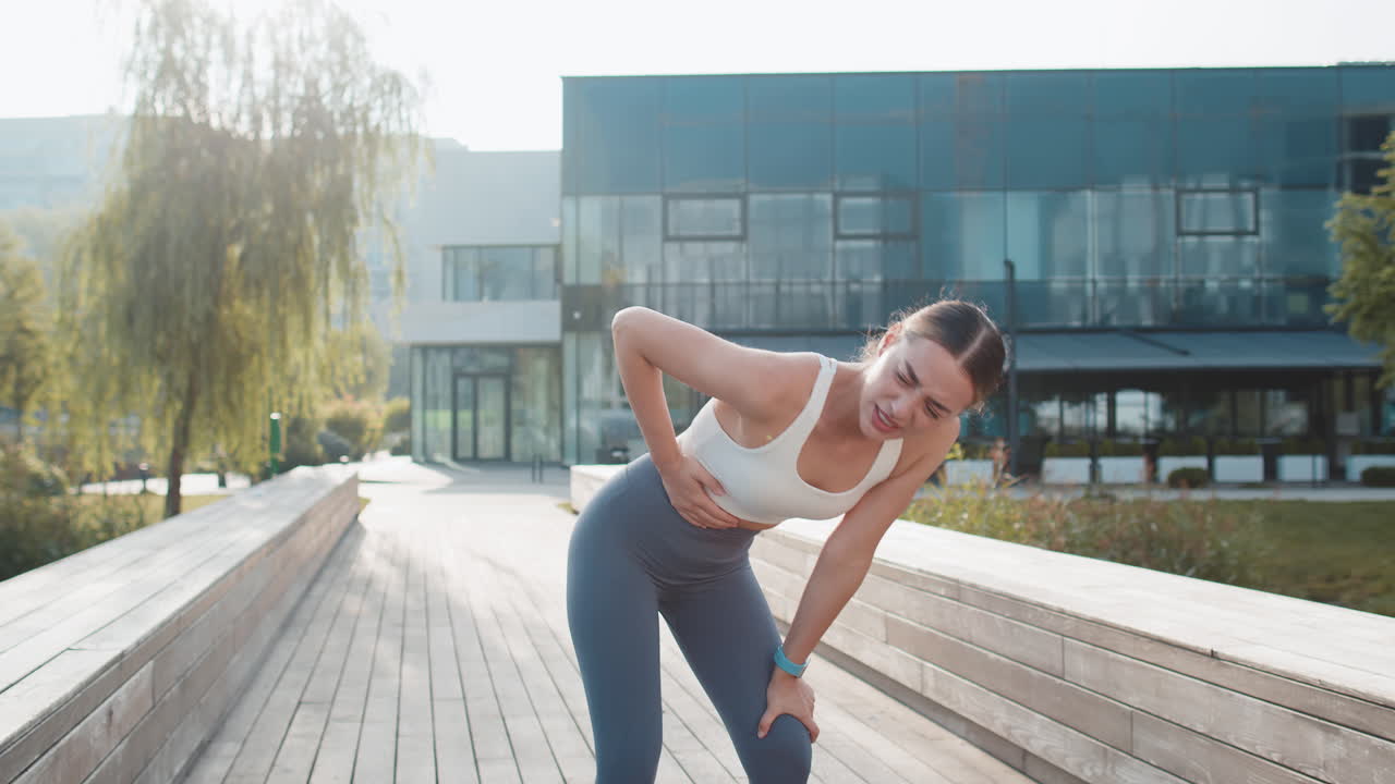 Young caucasian runner suffering from abdominal pain during a run in urban city park on sunny day