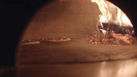 two-pizzas-cook-next-to-a-wood-burning-fire-in-a-neapolitan-style-pizza-oven