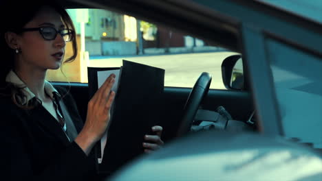 Attractive-caucasian-business-woman-in-a-parked-car,-going-over-paperwork,-rifling-through-her-documents-in-her-portfolio