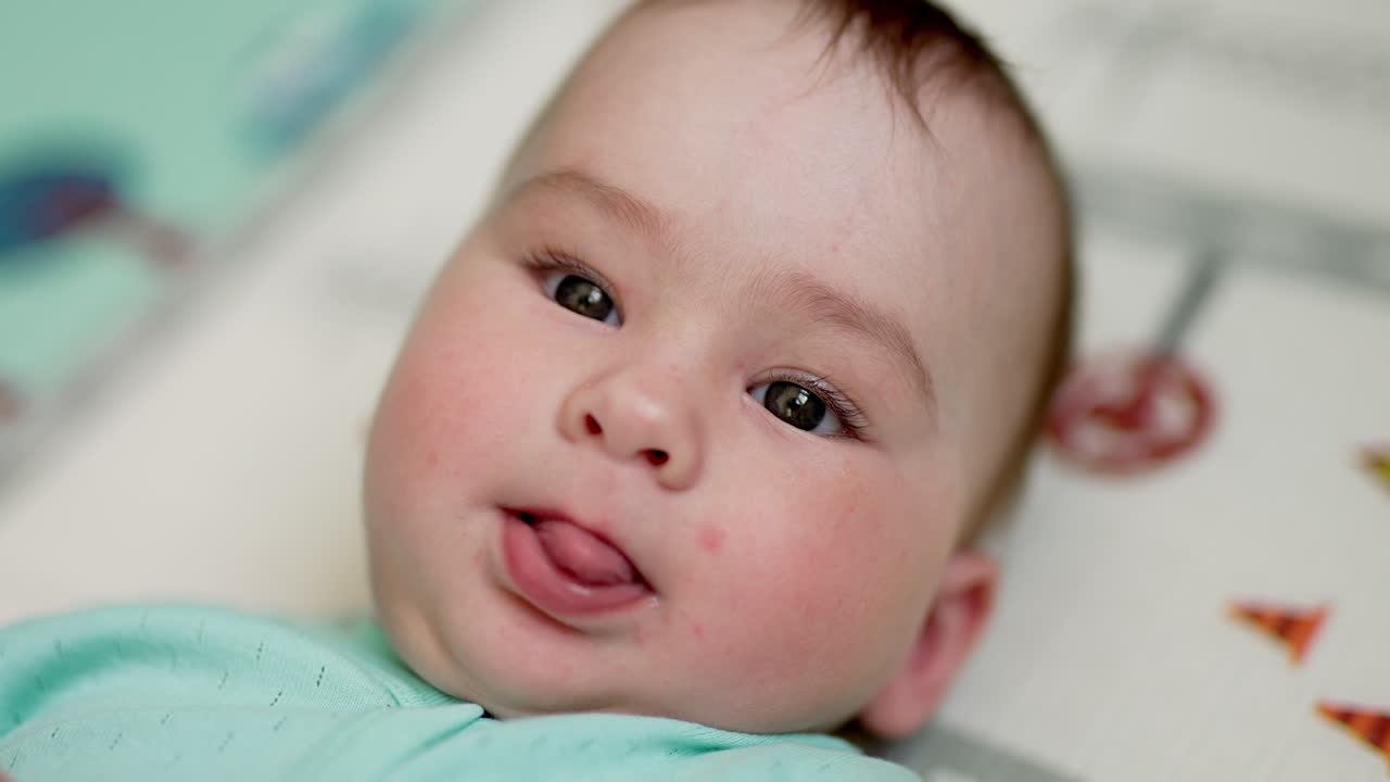 Beautiful dark-eyed baby lies peacefully on his back. Lovely kid with sweet cheeks showing tongue. Close up.