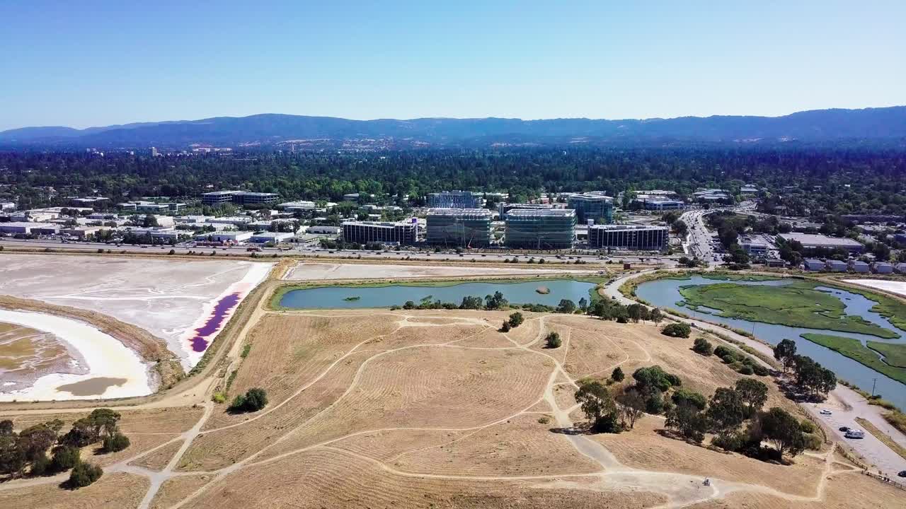 Aerial of dry grass at Bedwell bayfront park in menlo park with mounatins and corporate buildings in front, silicon valley, california USA