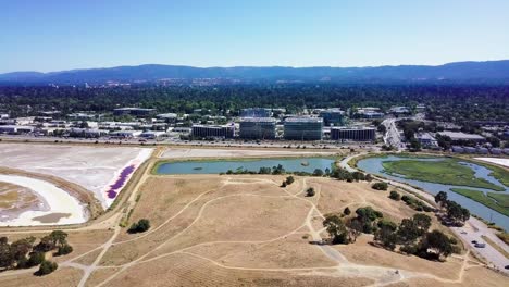 aerial of dry grass at bedwell bayfront park in menlo park with mounatins and corporate buildings in front, silicon valley, california usa