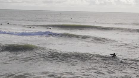 a surfer paddles out towards a group along the pier, sea, and group in the background