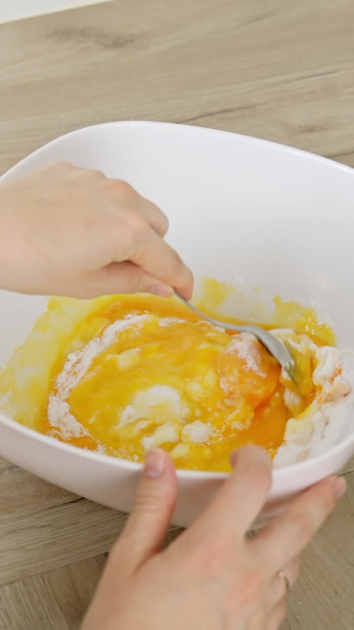 Vertical slow-motion shot of mixing egg yolk and powdered sugar with a spoon for tiramisu prep