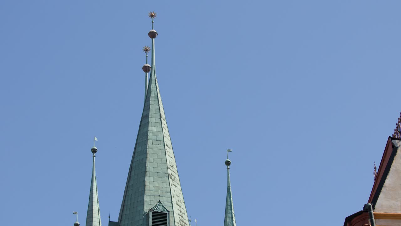Camera tilts upward past ornate streetlamp to reveal gothic church spires and clock tower, daylight