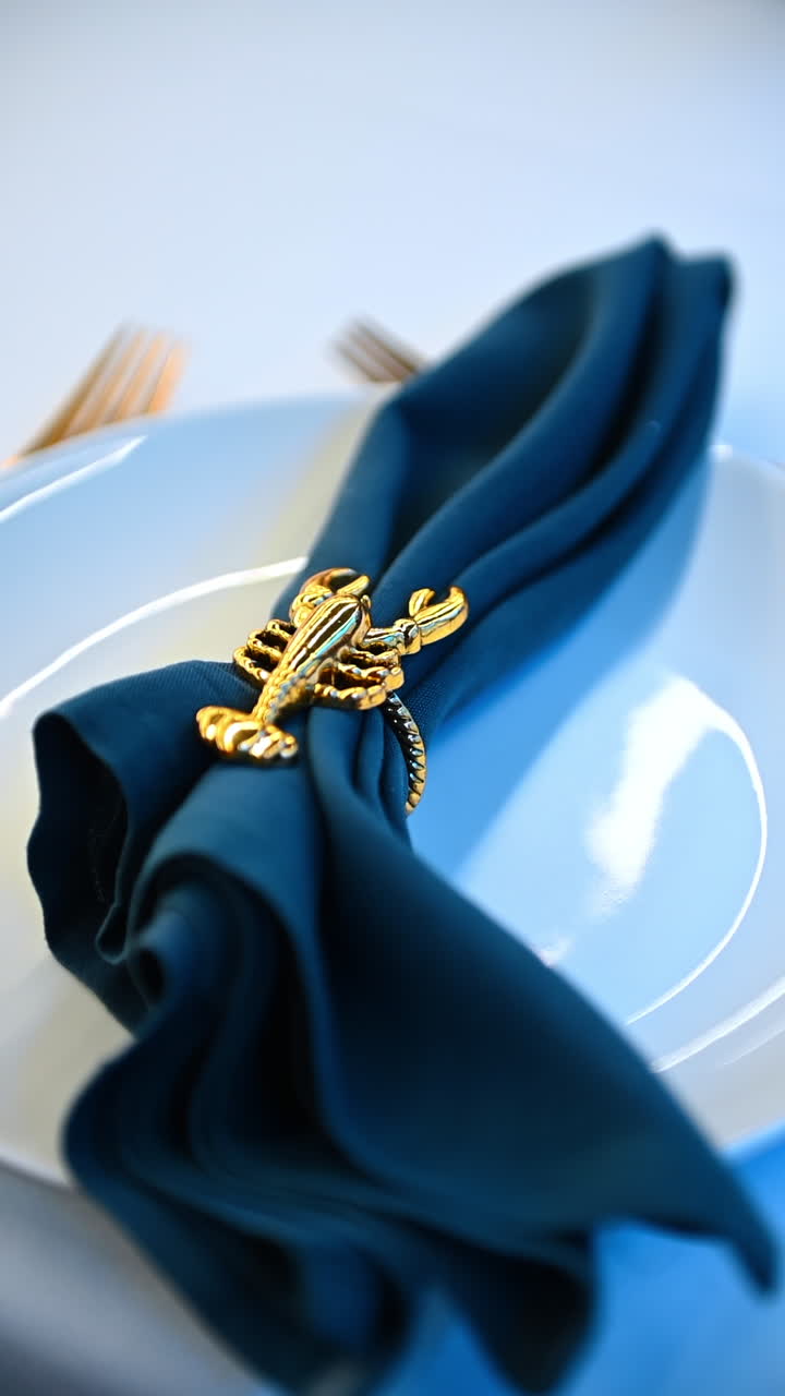 New York, USA, 8 August 2025: Golden lobster napkin ring. Golden lobster napkin ring placed on folded blue cloth on a plate