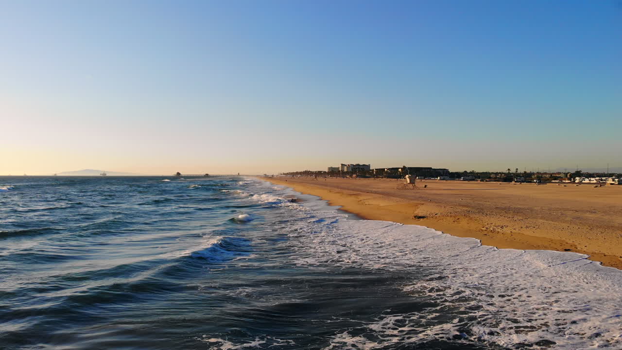 Fly right over surf line and waves and around to beautiful sunset over Pacific ocean at empty Huntington Beach, Southern California with aerial 4k DJI drone