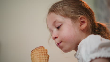 upward view of young girl enjoying ice cream cone, licking sweet treat with soft smile, casual indoor setting, sunlight highlighting hair, creating warm joyful moment of childhood
